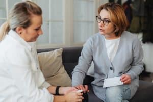 Two adult women sitting indoors having a thoughtful conversation on a couch.